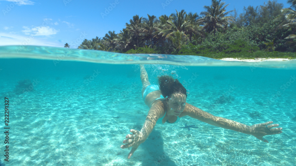 CLOSE UP: Cheerful woman squints while diving in the crystal clear Pacific ocean