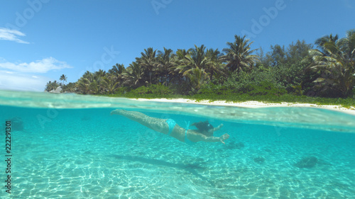 HALF UNDERWATER: Young woman on holiday diving in the crystal clear ocean water. © helivideo