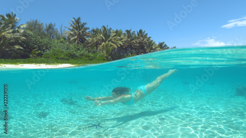 HALF UNDERWATER: Cheerful girl swimming underwater in the crystal clear ocean.