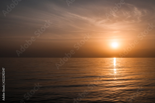 Golden natural sea sunset view of jetty or small bridge at horizon with people silhouette and orange sky landscape. Sunset or sunrise reflection in nature with sun in clouds above black sea scenery.