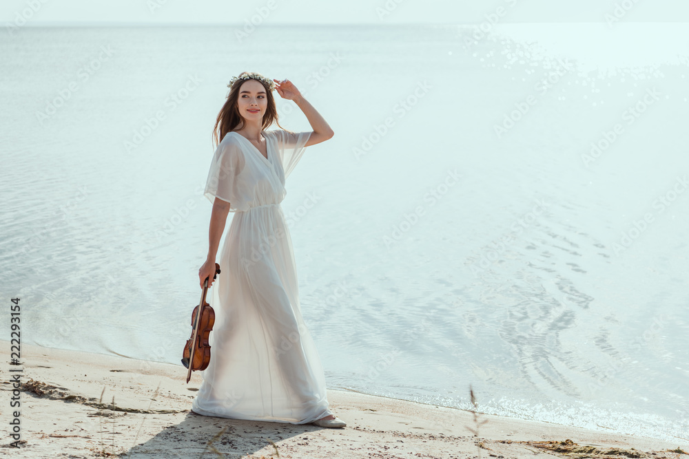 beautiful woman in elegant dress with violin walking on beach near sea beautiful woman in elegant dress with violin walking on beach near sea