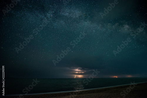 Starry night with thunderstorm and lightning over the sea
