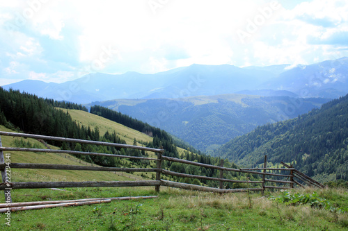 Beautiful landscape with view to wooden fence, pasture, forest and mountains.