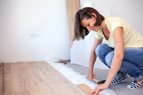 Happy young woman installing laminate flooring in new apartment. Holding a hammer. Home improvement and renovation concept
