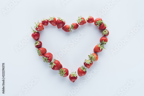 top view of heart shape sign made of fresh strawberries on white surface