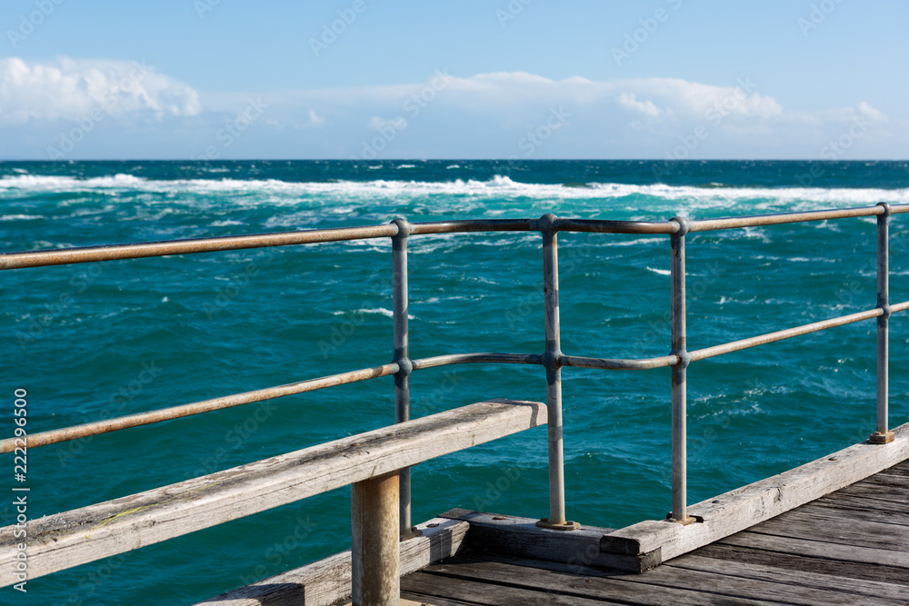 A bench seat on the Port Noarlunga Jetty looking out to the rough seas and reef in South Australia on 6th September 2018