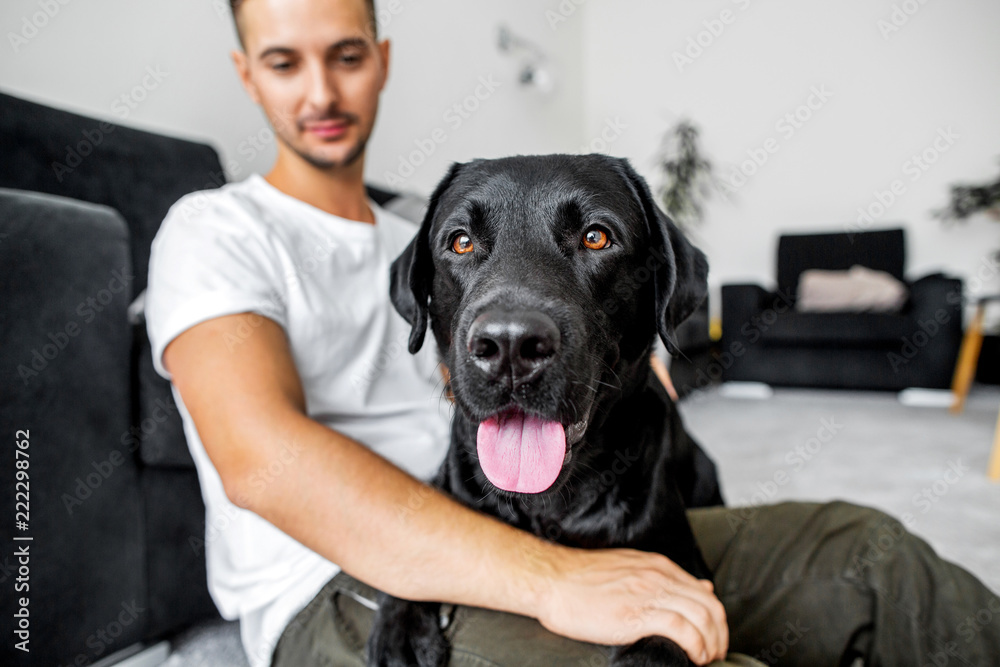 freelancer guy sitting at home working with a dog in an embrace, black labrador. freelancer guy sitting at home working with a dog in an embrace, black labrador.