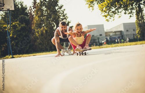 Little girl on skateboard .Father behind.