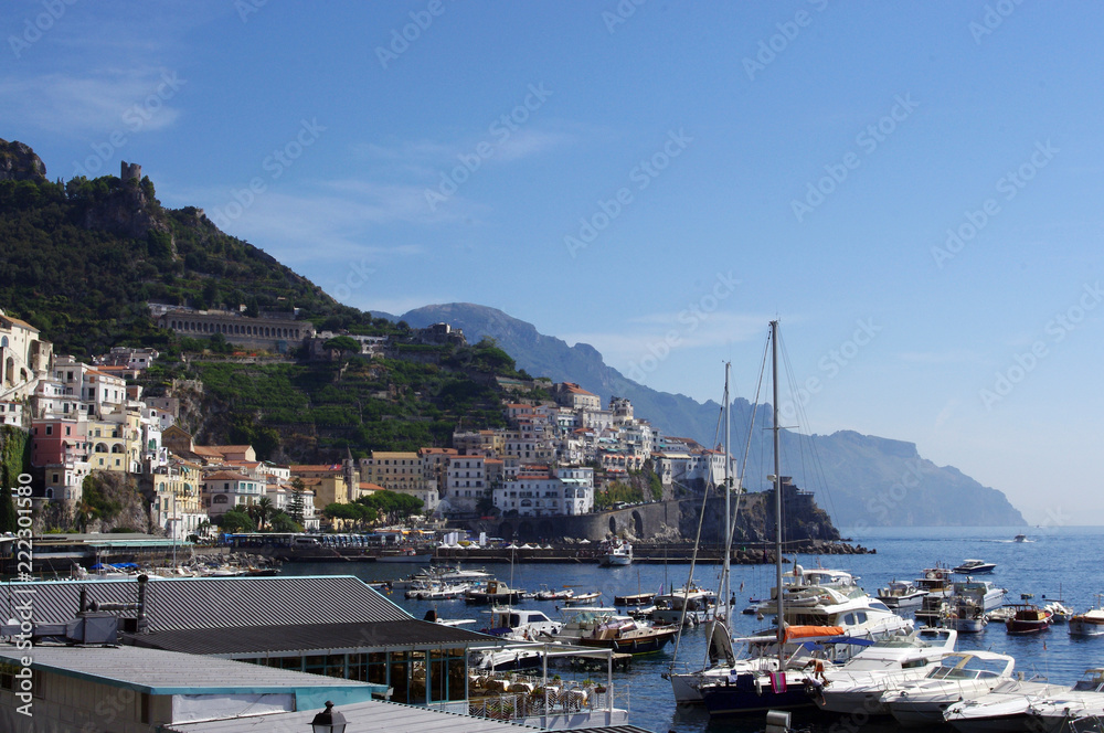 View of Amalfi across boats in harbour to mountains, Italy