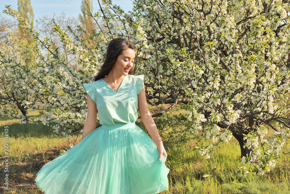 Beautiful young woman near blossoming tree on sunny spring day