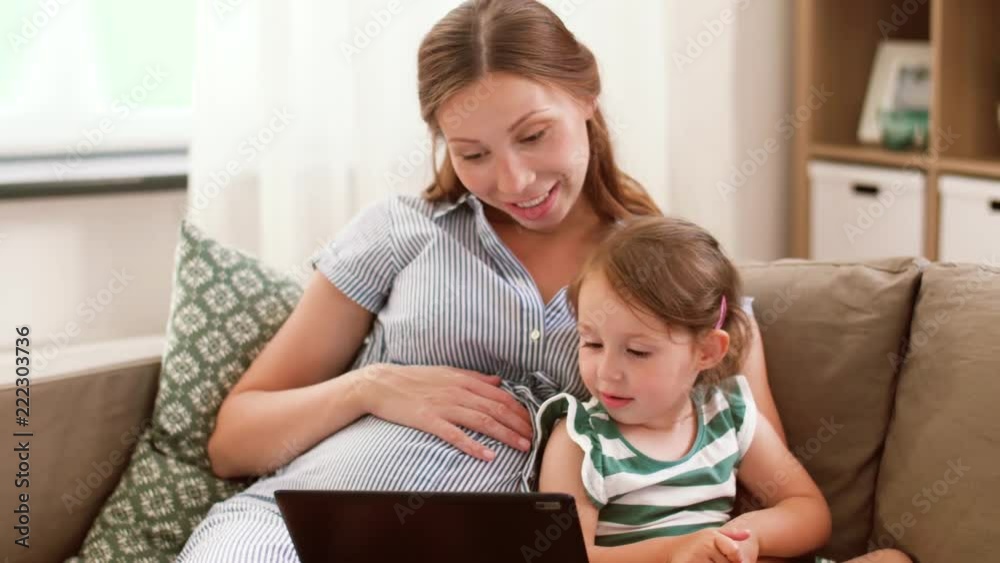 pregnancy, technology and family concept - happy pregnant mother and little daughter with tablet pc computer at home pregnancy, technology and family concept - happy pregnant mother and little daughter with tablet pc computer at home