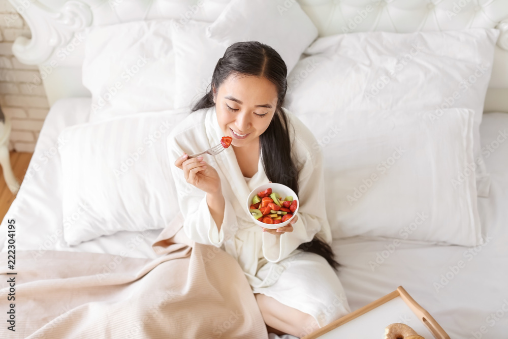 Asian woman eating healthy fruit salad for breakfast at home