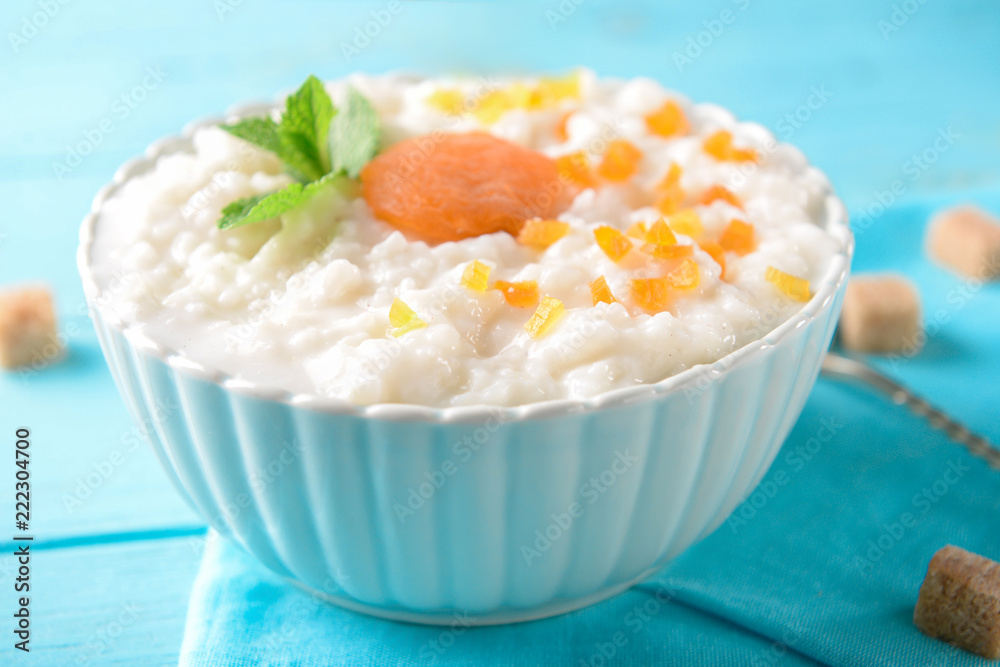 Bowl with delicious rice pudding and dry apricots on color table Bowl with delicious rice pudding and dry apricots on color table