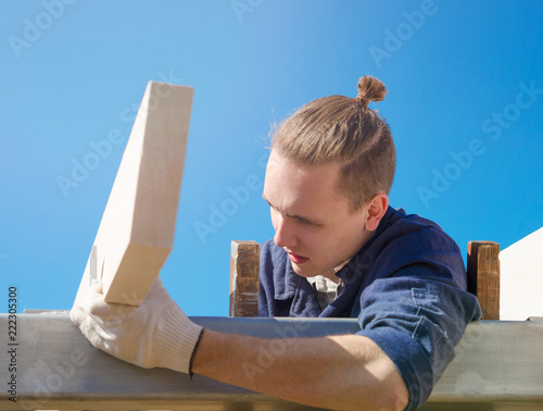 A focused young man in gloves and work clothes is building a roof