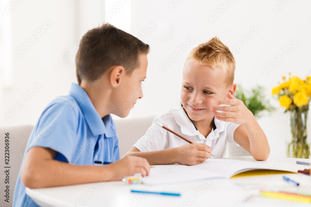 Two smiling little boys drawing in the notebook and talking to each other. Two smiling little boys drawing in the notebook and talking to each other.