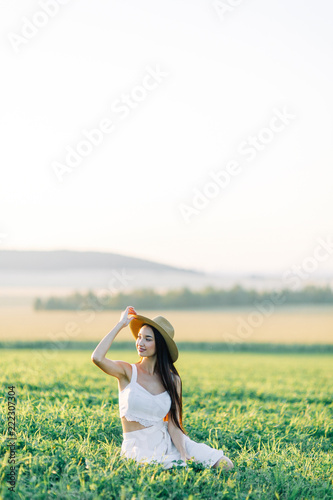 Girl walking on the field, in a hat and summer dress. Smiling and laughing, beautiful sunset in the forest and in nature. Happy traveler, lifestyle.