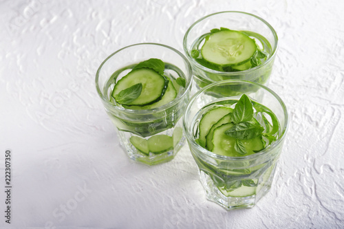 Glasses of cucumber infused water on white textured background