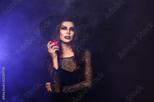 Beautiful woman dressed as witch for Halloween with apple on dark color background