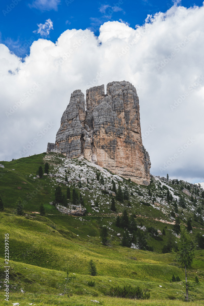 Famous Dolomiti landmark, Cinque Torri. Rock towers in green meadows and pastures of Dolomiti, blue sky with dramatic clouds. Trekking, hiking and climbing area. Alpine landscape.