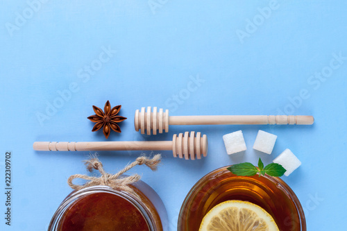 Tea drinking. A cup of hot tea with a slice of fresh mint and a juicy lemon, honey jar and honey spoons, rafinated sugar, anisetree on a blue background. Top view. Copy space photo