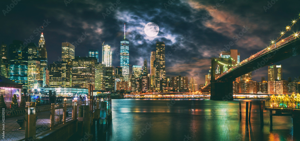 New York City Brooklyn Bridge and Manhattan skyline illuminated at night with full moon overhead.