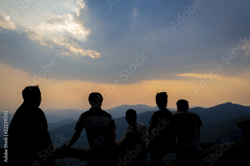 Silhouettes of a group of people watching the sunset from a mountaintop with mountain ranges in the distance as background