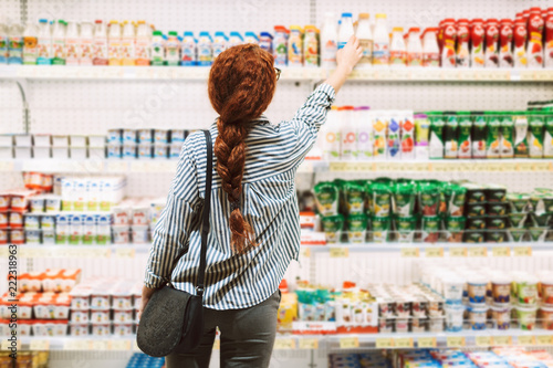 Pretty girl in striped shirt from back choosing dairy products in supermarket