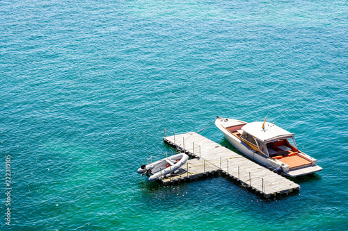 A luxury speedboat moored to an isolated, t-shape, wooden dock in green waters with an inflatable dinghy laying on the dock. photo