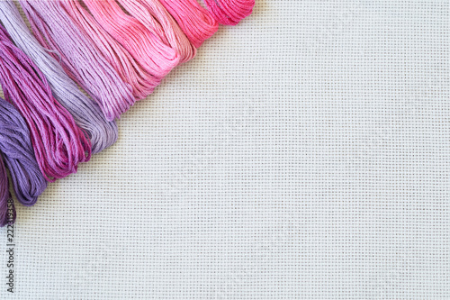 White fabric for cross stitch embroidery and a bunch of colorful threads with a place for copy