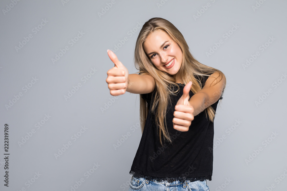 Confident young woman giving the thumbs up against a gray background Confident young woman giving the thumbs up against a gray background