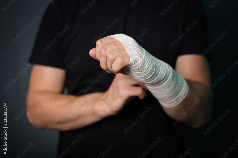 Fotka „A young handsome guy in a black T-shirt with a bandaged hand on a  gray background. A man with a hand in a bandage bandage.“ ze služby Stock |  Adobe Stock
