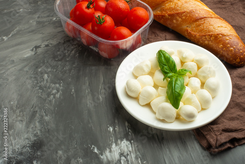 Mozzarella with basil leaves - fresh ingredients for Bruschetta, with cherry tomatoes and French baguette with copy space on a dark background, top view photo