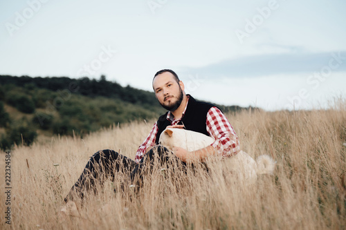 a male hipster sits in a park with a dog