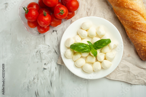 Mozzarella with basil leaves - fresh ingredients for Bruschetta, with cherry tomatoes and French baguette with copy space on a light background, top view photo