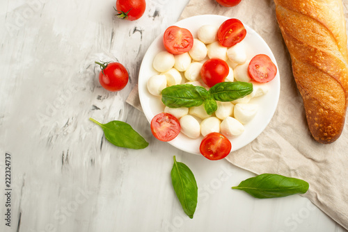 Mozzarella with basil leaves - fresh ingredients for Bruschetta, with cherry tomatoes and French baguette with copy space on a light background, top view photo
