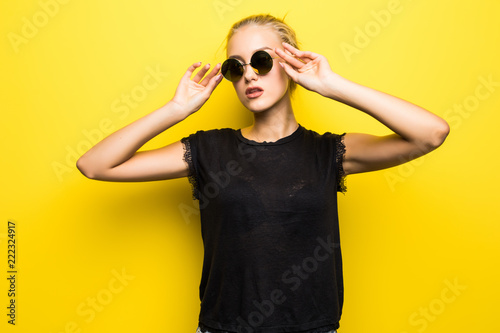 Portrait of smiling beautiful girl in sunglasses against yellow background
