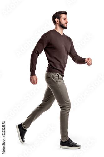 A young bearded man in a side view walks fast on the verge of running on a white background.