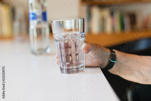 Hand of senior lady holding a glass of water on table