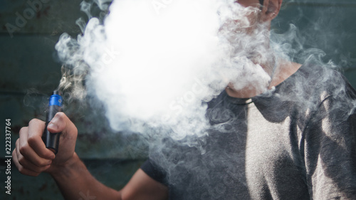 man vaping with the vapor cloud on grunge background © pavelkant