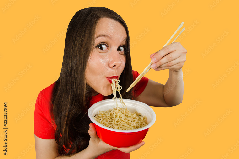 Young girl in a red t-shirt eats chinese noodles with chopsticks isolated on a orange background.