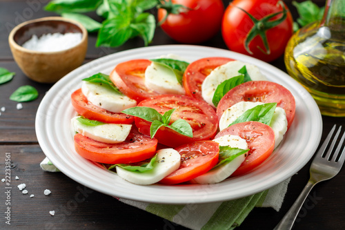 Italian caprese salad with tomatoes, mozzarella cheese and basil in plate on dark wooden background photo