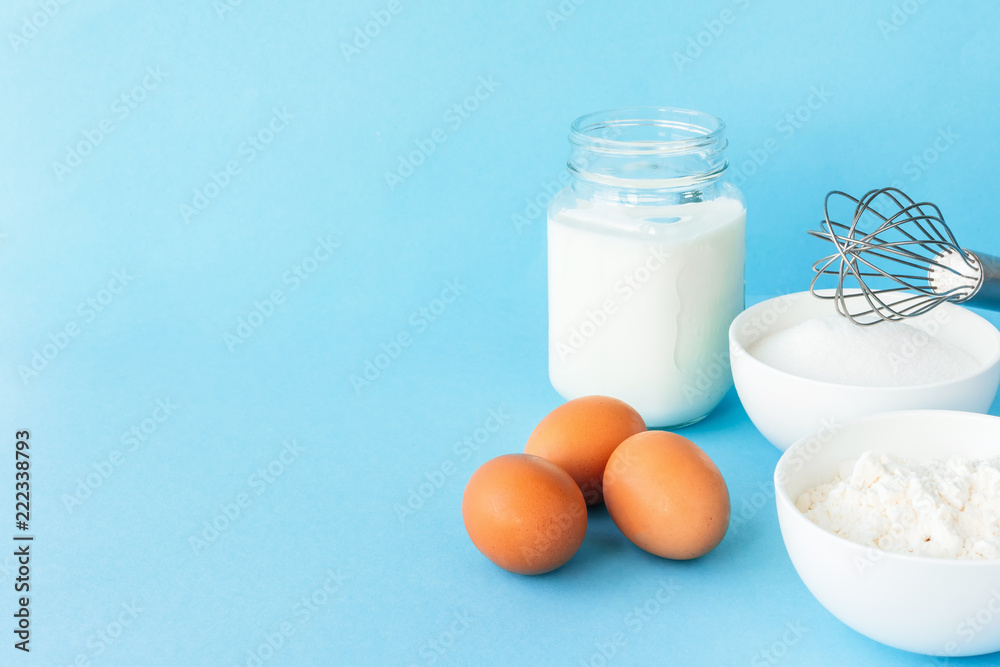 Eggs, flour, milk, sugar, and various ingredients for making pastry homemade pastry on a blue background with copy space