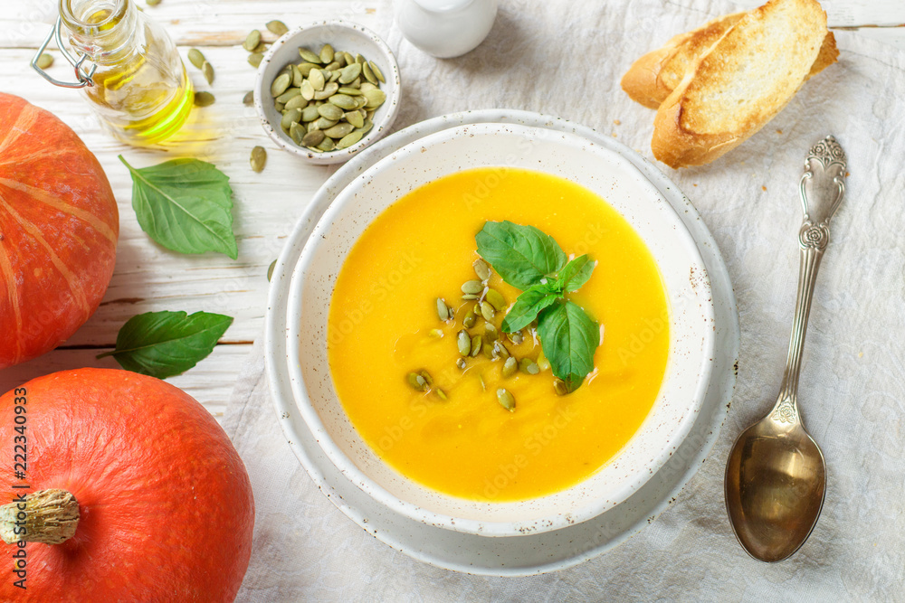 Dietary vegetarian pumpkin cream soup puree with olive oil, seeds and Basil on a light wooden table in a white plate Dietary vegetarian pumpkin cream soup puree with olive oil, seeds and Basil on a light wooden table in a white plate