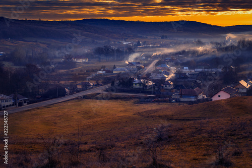 Beautiful rural scene with a village in a valley surrounded by smoke from the horns and fog during the winter