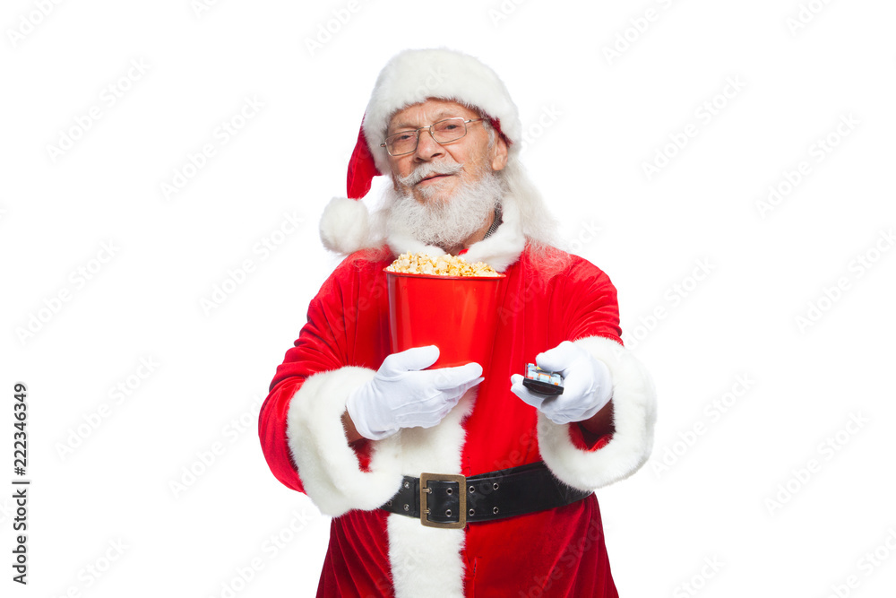 Christmas. Smiling, good Santa Claus in white gloves holding a red bucket of popcorn in one hand, and a TV remote control with his second hand and switches channels. The concept of watching a movie Christmas. Smiling, good Santa Claus in white gloves holding a red bucket of popcorn in one hand, and a TV remote control with his second hand and switches channels. The concept of watching a movie