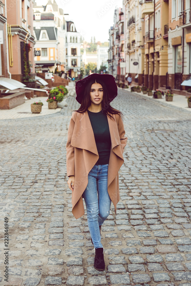 Autumn fashion. Full length of beautiful young woman in stylish hat and coat looking at camera while standing outdoors