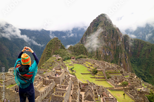 Female tourist gesturing a love sign to the famous ancient Inca ruins of Machu Picchu, Cusco, Peru