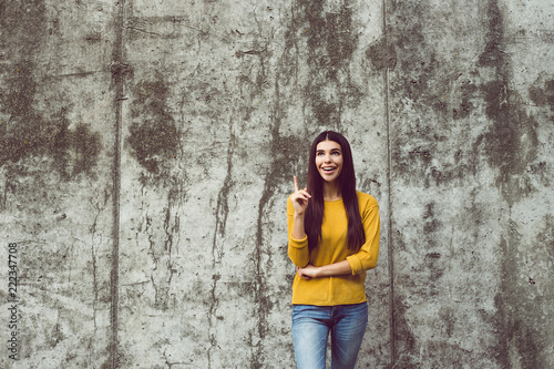 I have an idea! Beautiful young woman looking at camera with smile while standing against concrete background outdoors 
