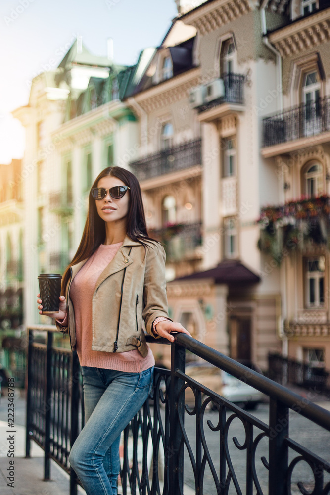 Beautiful lovely day. Full length of beautiful young woman in sunglasses holding coffee cup and looking at camera with smile while standing outdoors
