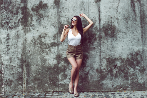 Sexy mood today. Full length of beautiful young woman looking away with smile while standing against concrete background outdoors 